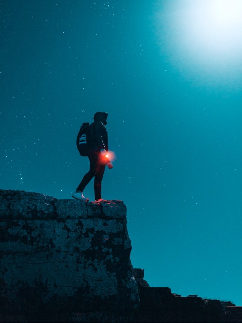 Hiker on cliff under starry night sky symbolizing elite adventure travel