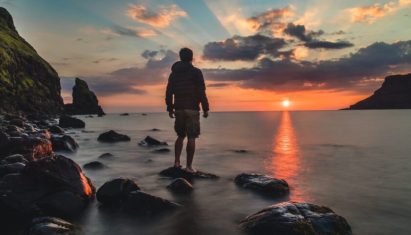 Traveler standing on ocean rocks watching sunset for luxury coastal adventure